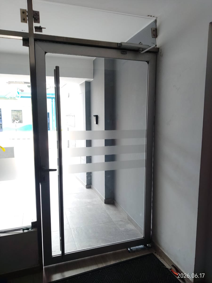 Puerta de vidrio transparente con marco oscuro y tirador vertical.